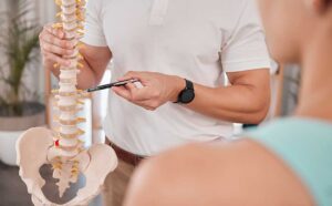 Clinician guiding an adult through gentle back mobility exercises in a bright treatment room.