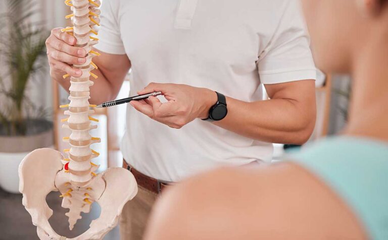 Clinician guiding an adult through gentle back mobility exercises in a bright treatment room.