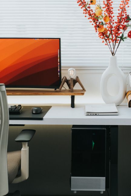 Person seated at a desk with a raised monitor, supported lower back, relaxed shoulders, and feet flat on the floor.